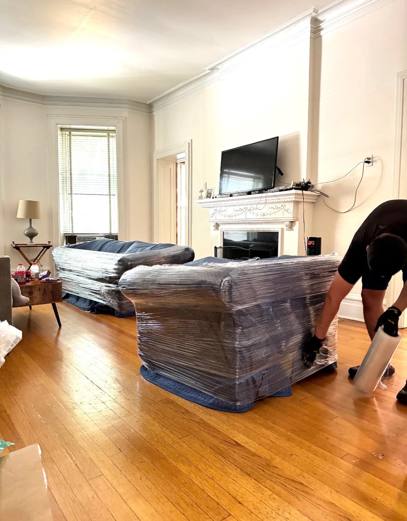 A MoveMax mover shrink-wrapping a padded sofa in a living room